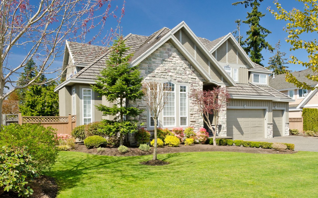 Two-story stone-and-stucco house with multiple gables, an attached garage, and landscaped front yard.