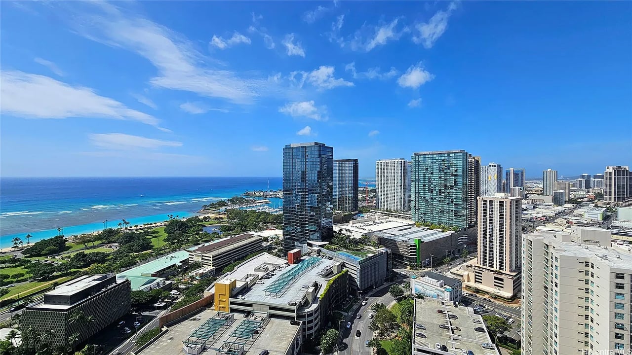 Panoramic view of Honolulu high-rises, shoreline, and Pacific Ocean from above.