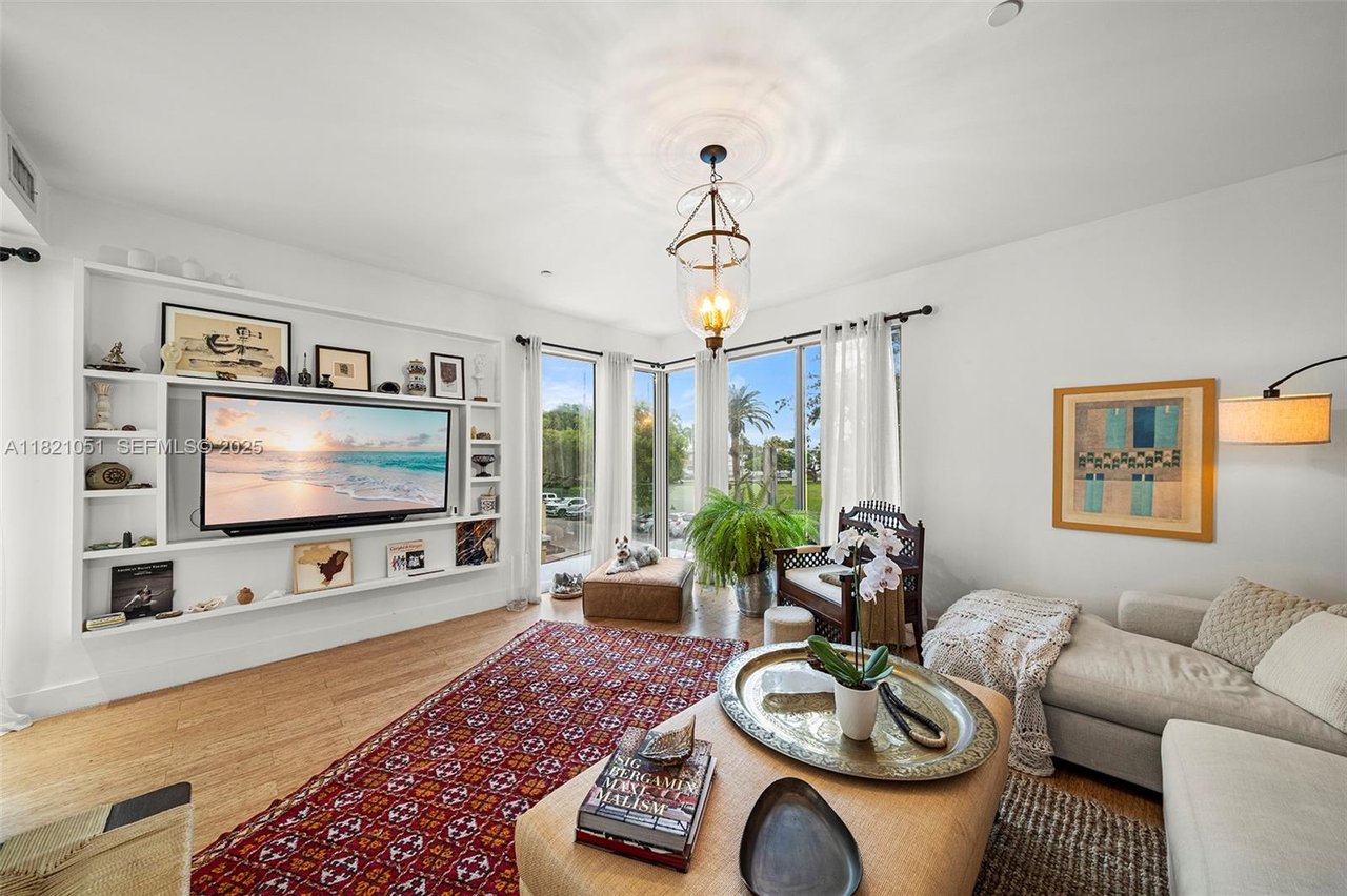Living room with built-in media shelving, corner windows, hardwood floors, and a red patterned rug.