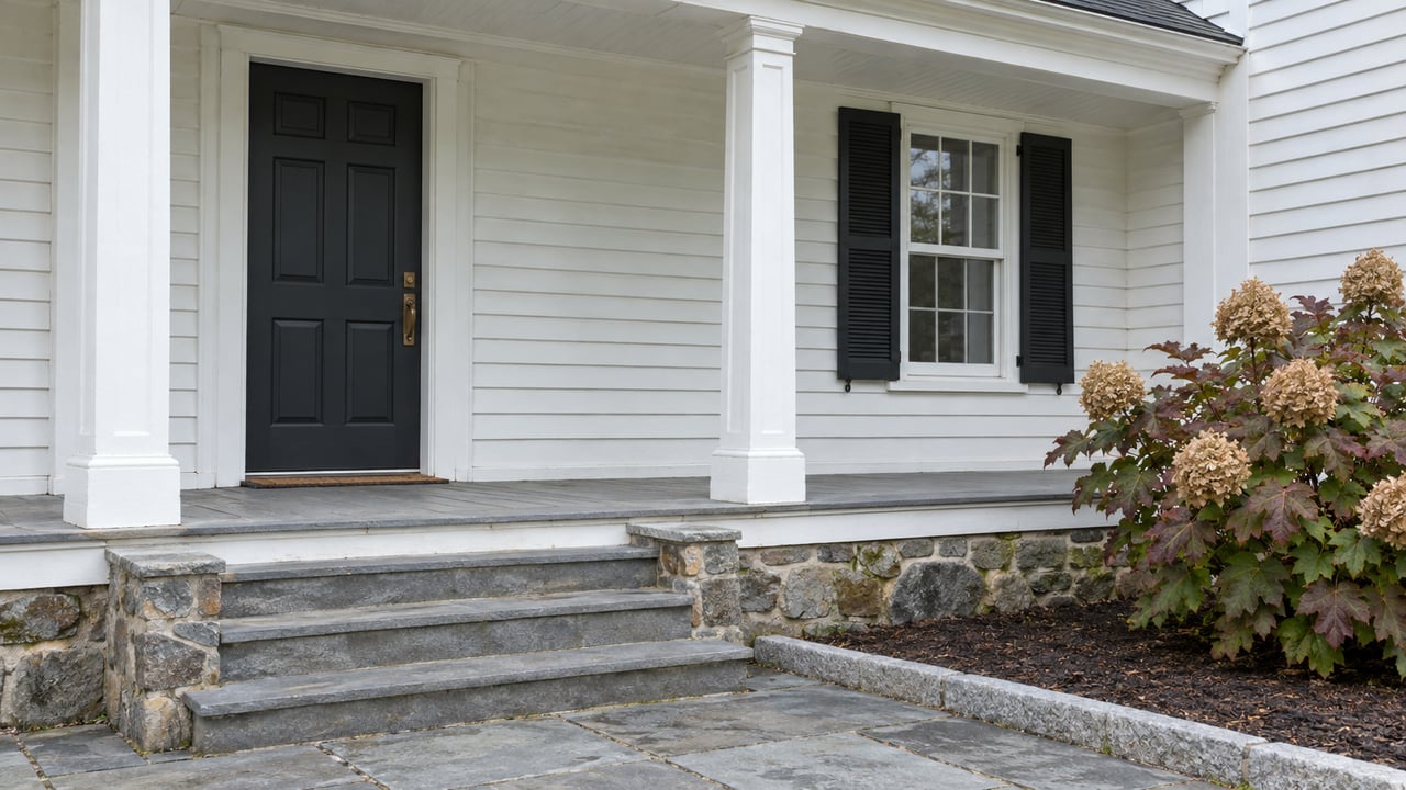White clapboard porch with black shutters, worn bluestone steps, fieldstone foundation and autumn oakleaf hydrangea.