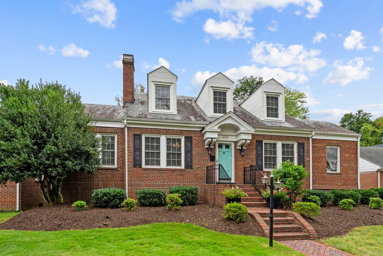 Red-brick home with three dormers, a turquoise front door, and landscaped brick steps.