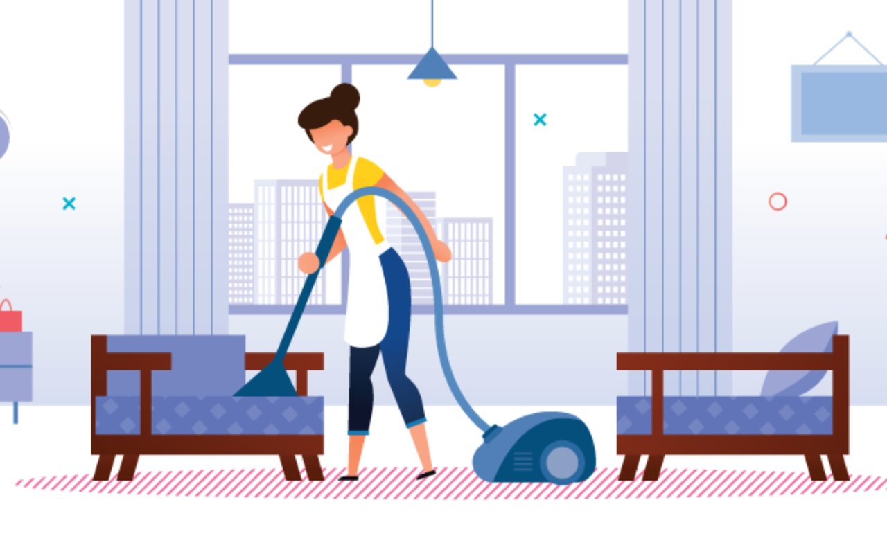 A woman vacuums the floor between two sofas in a bright living room.