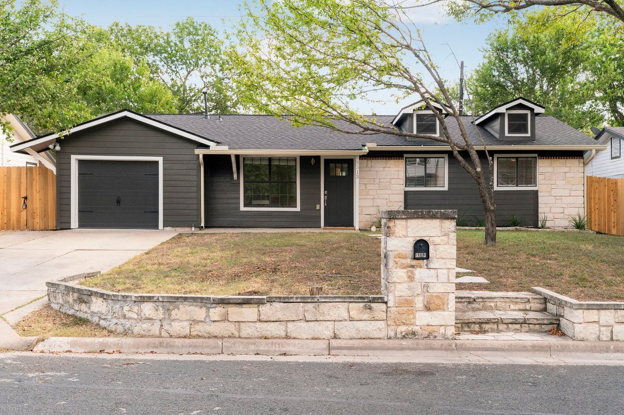 Single-story gray house with stone facade, attached garage, dormers, and a stone mailbox pillar.