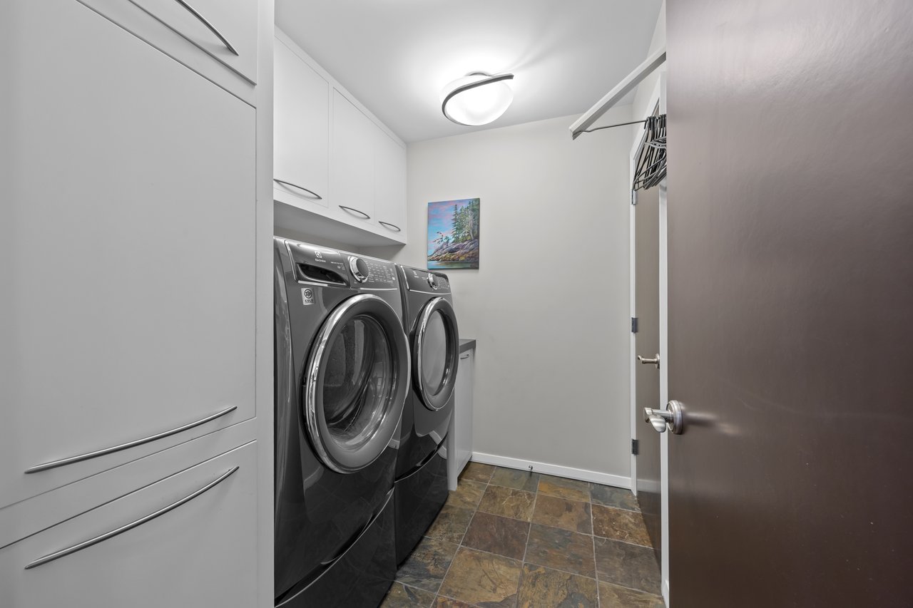 Laundry room with dark front-loading washer and dryer beneath white built-in cabinets.