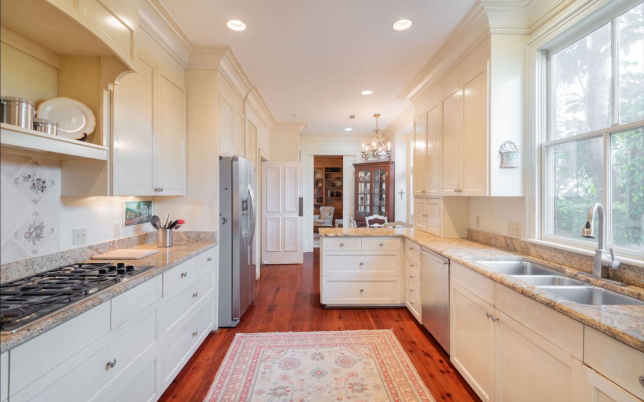 Bright white kitchen with granite counters, stainless appliances, and a double sink beneath a large window.