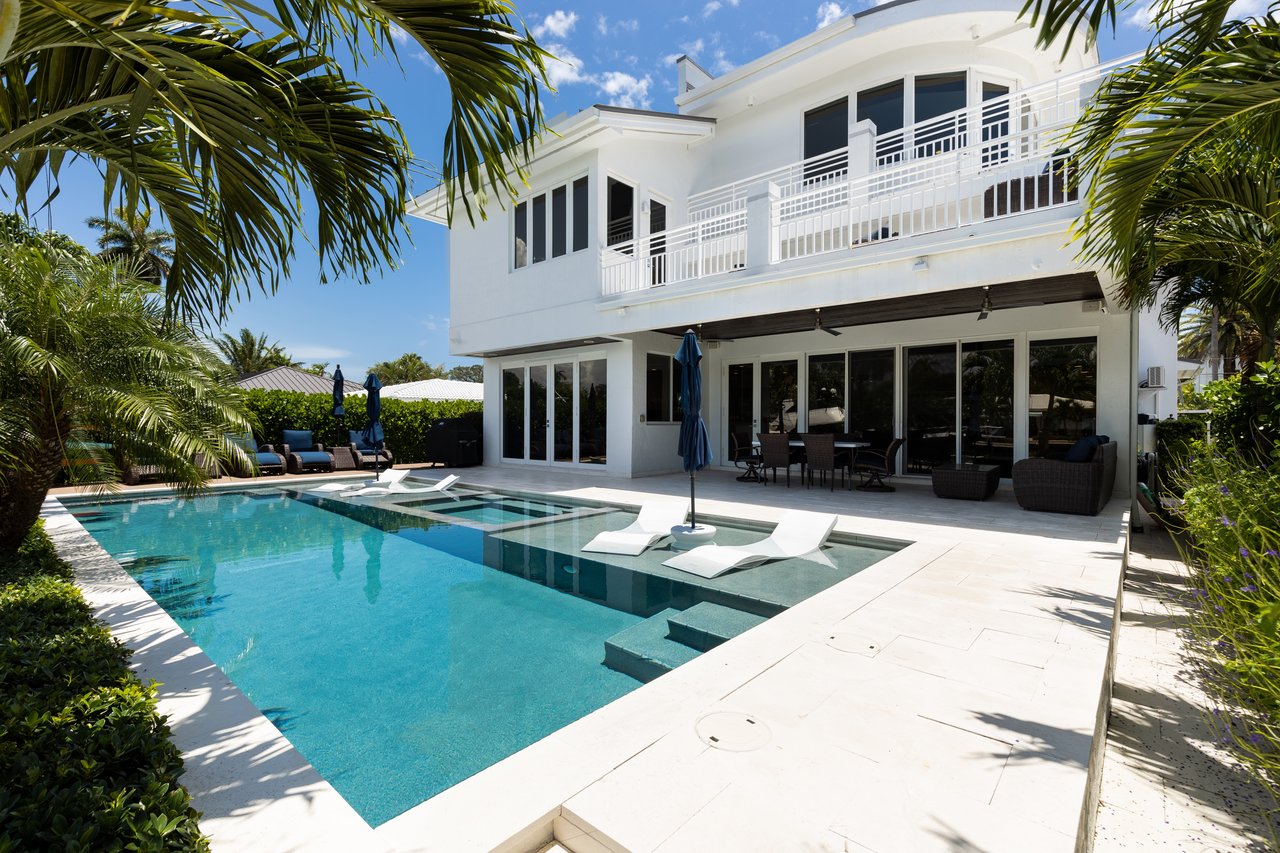 Modern white home behind a swimming pool with submerged loungers and palm-framed patio.
