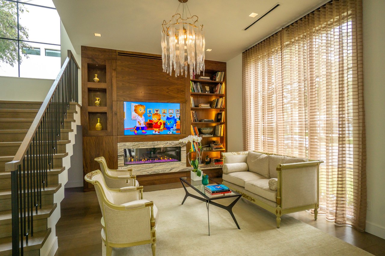 Seating area by a floating staircase, hanging glass chandelier, and stunning wood wall with cabinets, fireplace, and TV.