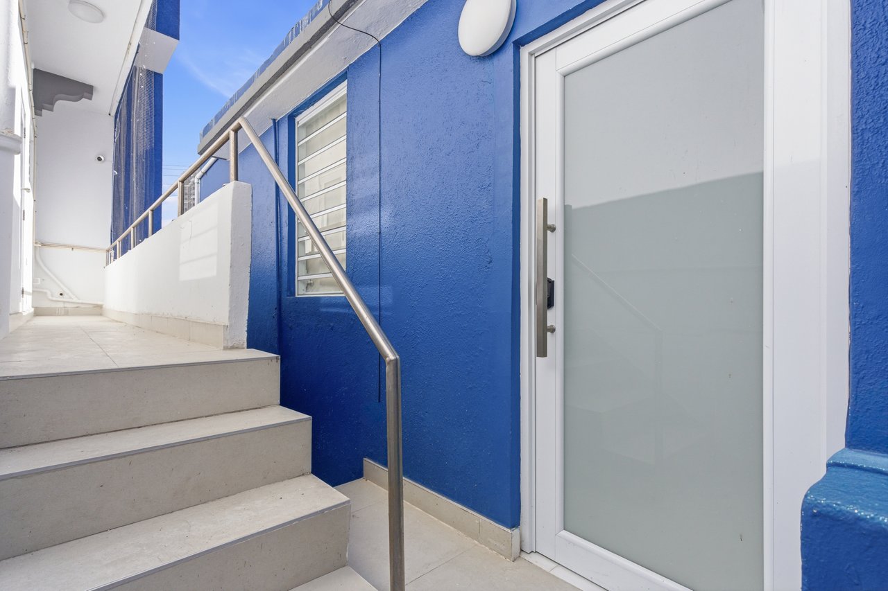 Blue building entrance with concrete steps, metal handrail, and frosted-glass door.