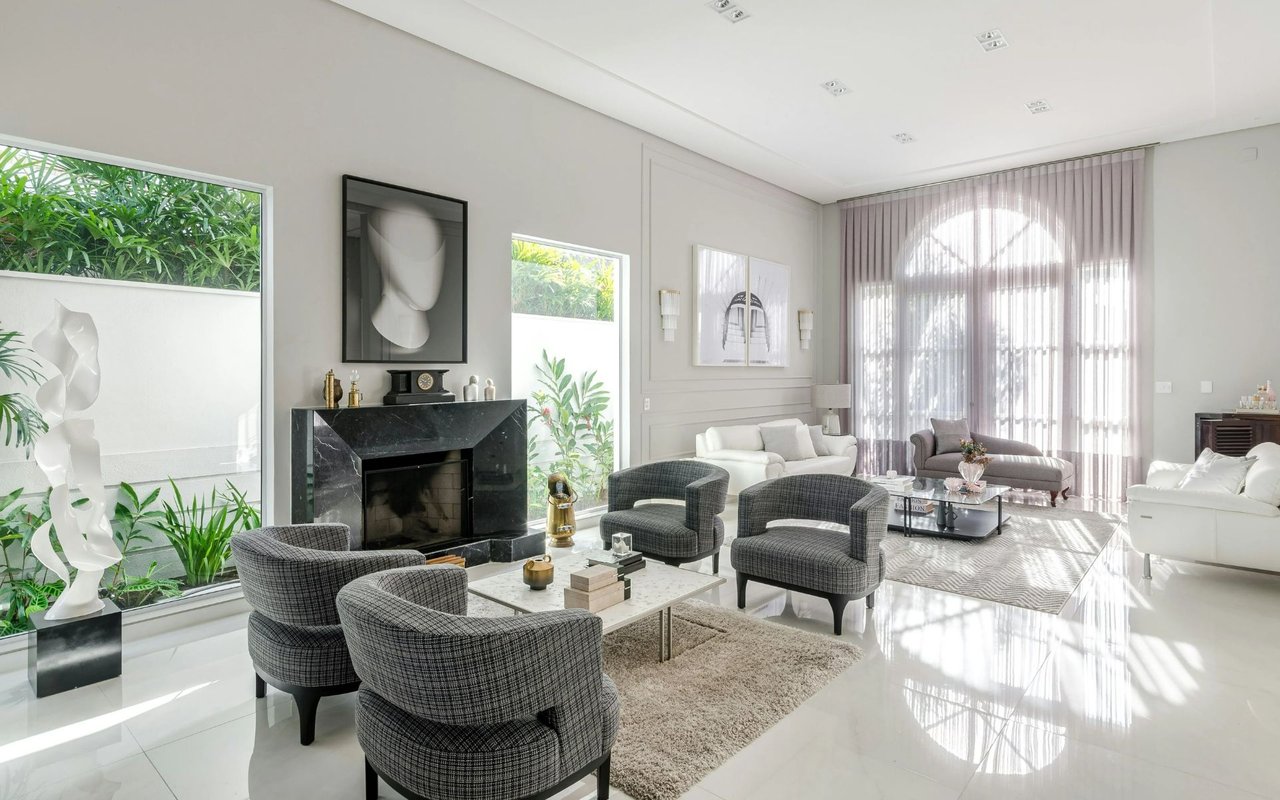 Bright living room with a marble fireplace, patterned chairs, and tall arched windows.