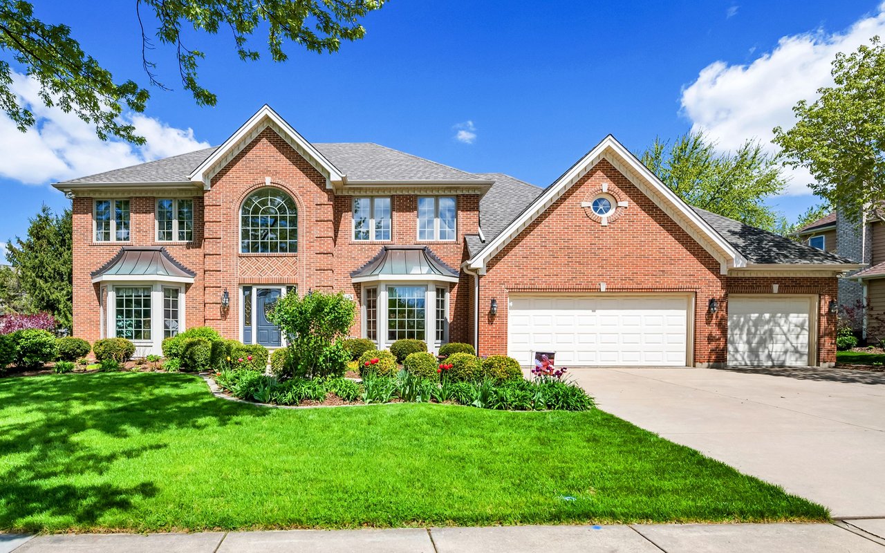 Two-story red brick house with an arched window, landscaped lawn, and two garages.