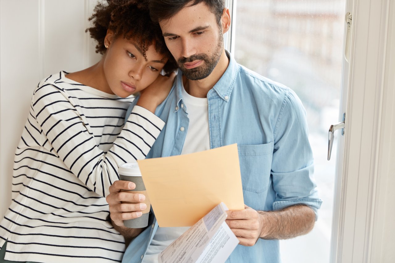 Concerned couple reviewing paperwork and calculating finances, highlighting the impact of hidden fees in real estate transactions.