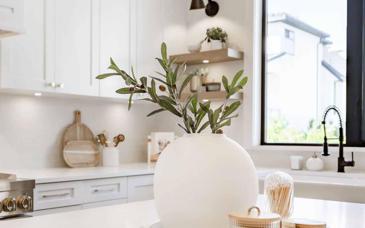 Bright white kitchen with black faucet, large window, and a vase of leafy branches.