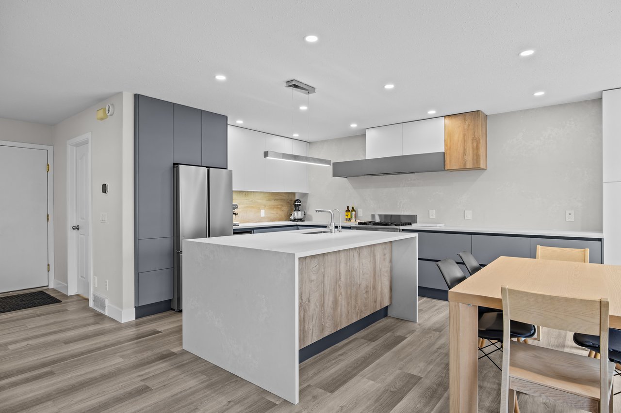 Modern kitchen with a large waterfall island, gray cabinets, and an adjacent light wood dining table.