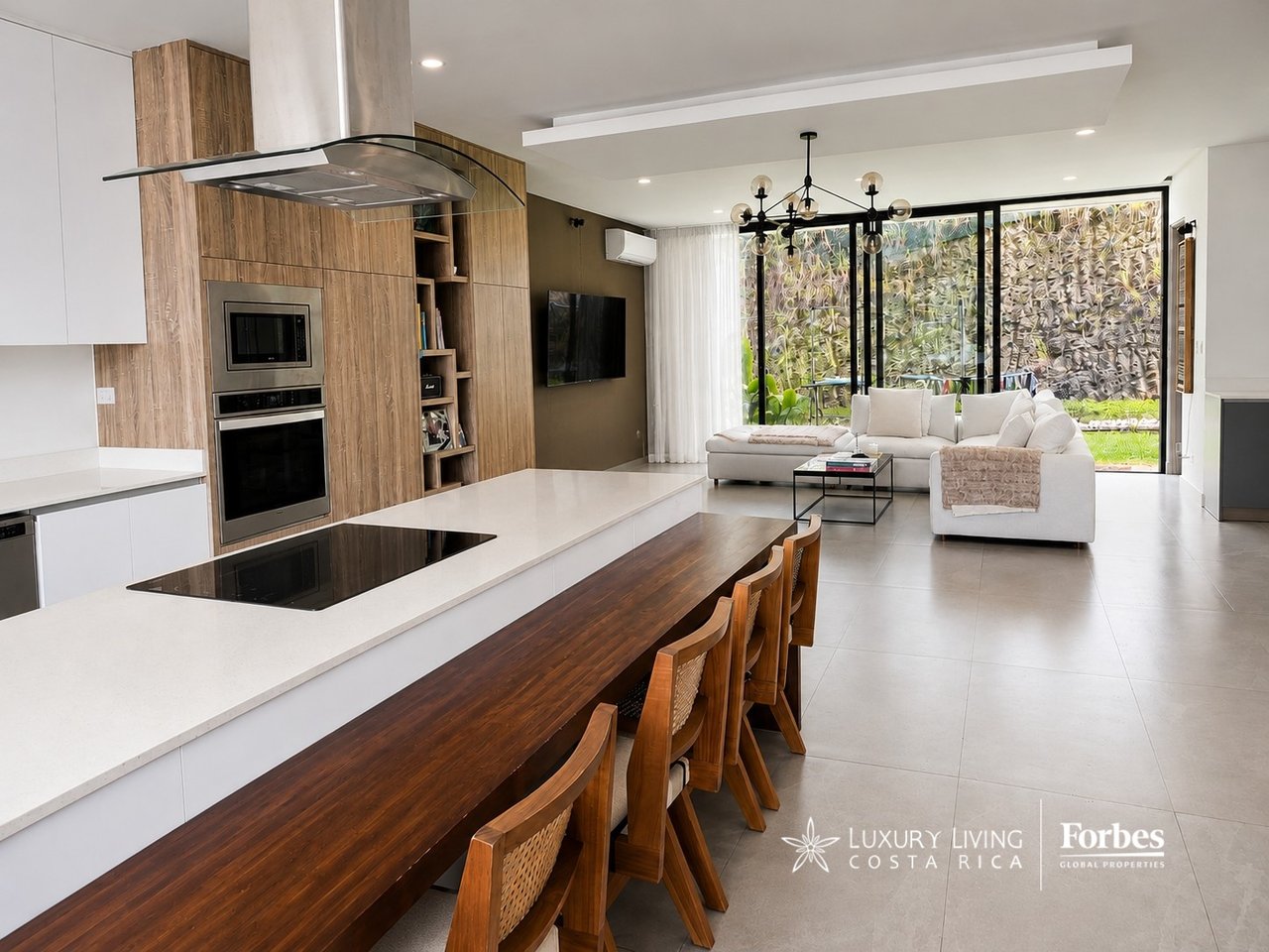 Open-plan kitchen and living room with a long wood dining counter, white sectional, and garden-facing glass doors.