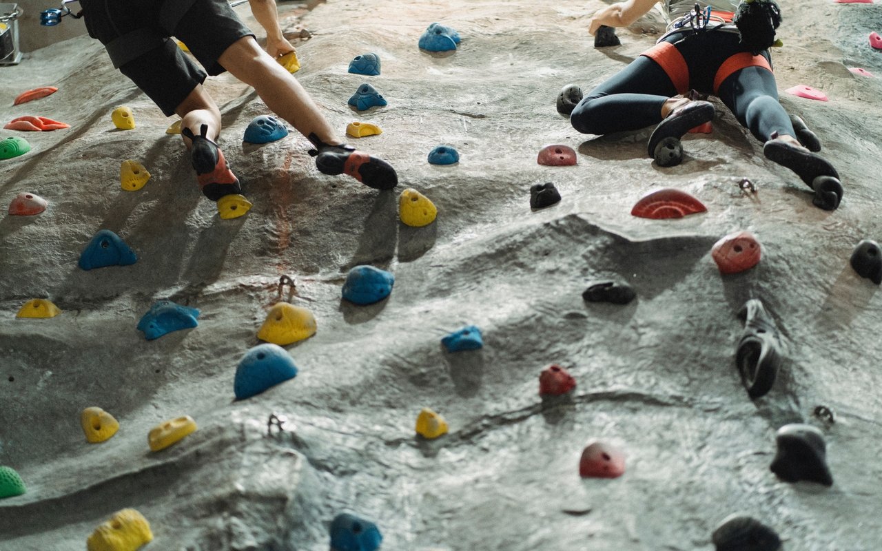 Two climbers scale an indoor bouldering wall dotted with colorful holds.