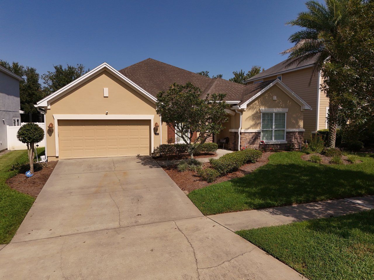 Tan single-story home with a two-car garage, stone accents, and a landscaped front yard.