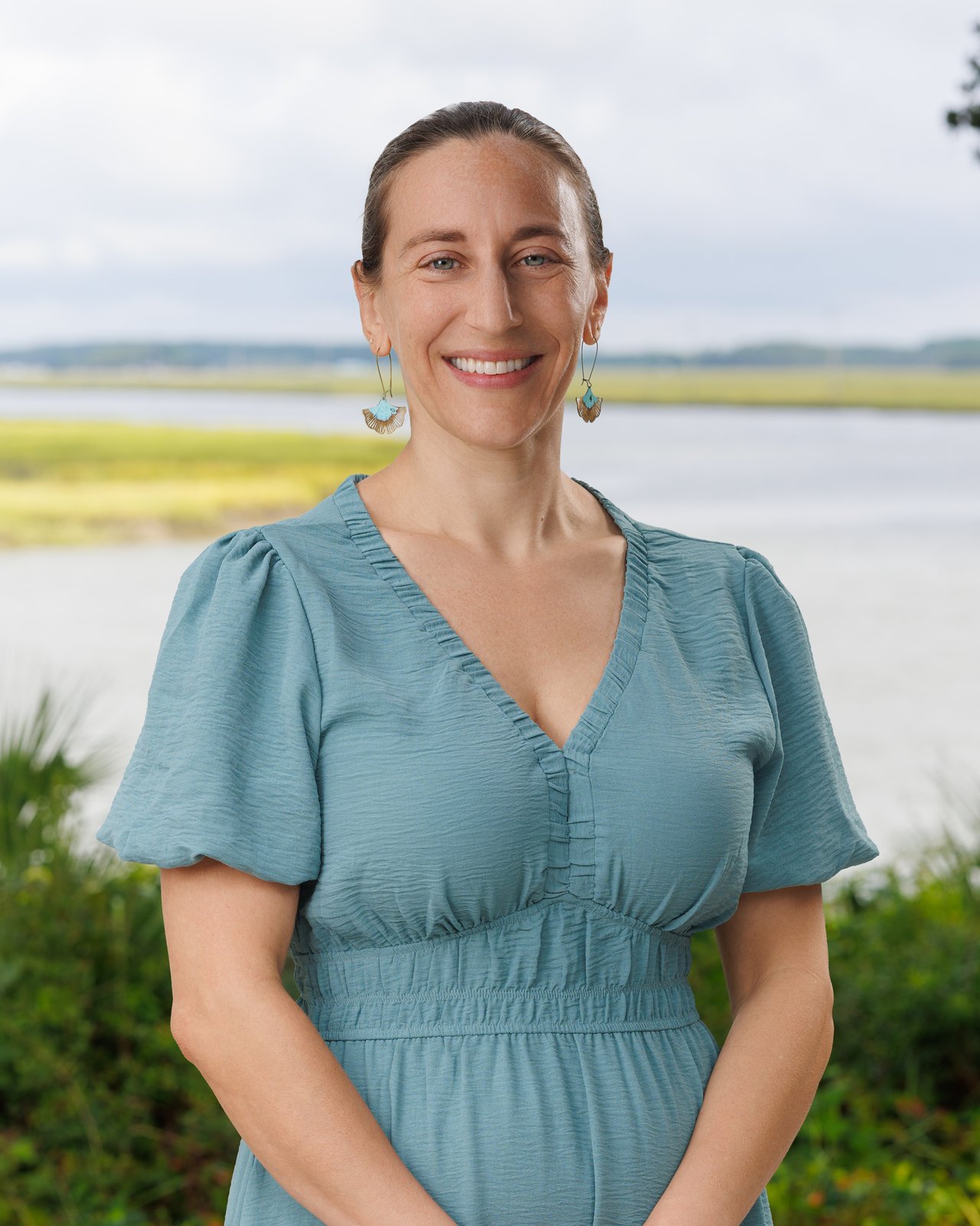 Rikki Peluso smiling in a blue dress beside a marsh.