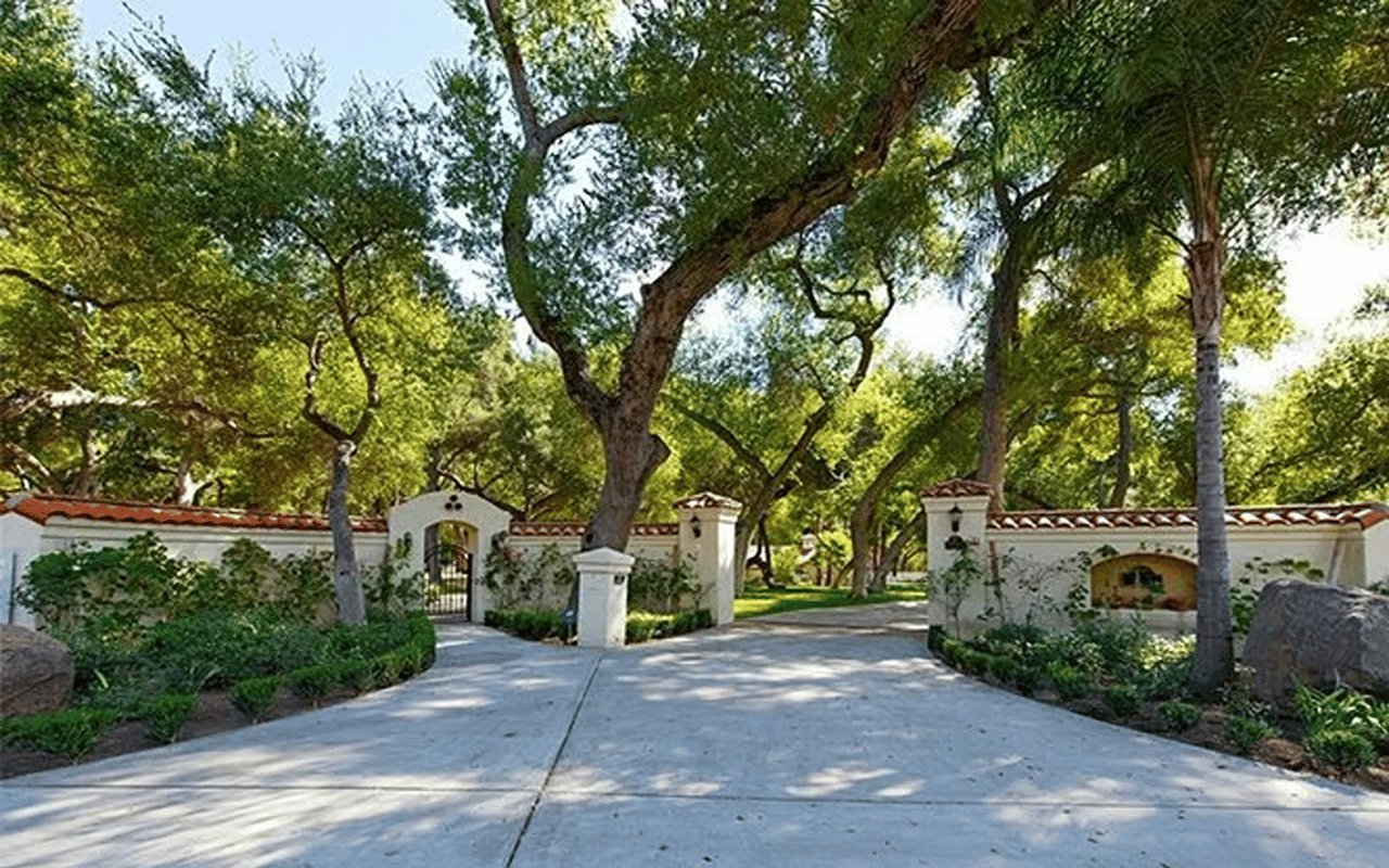Landscaped entrance with a gated archway, red tile roof caps, and mature trees.