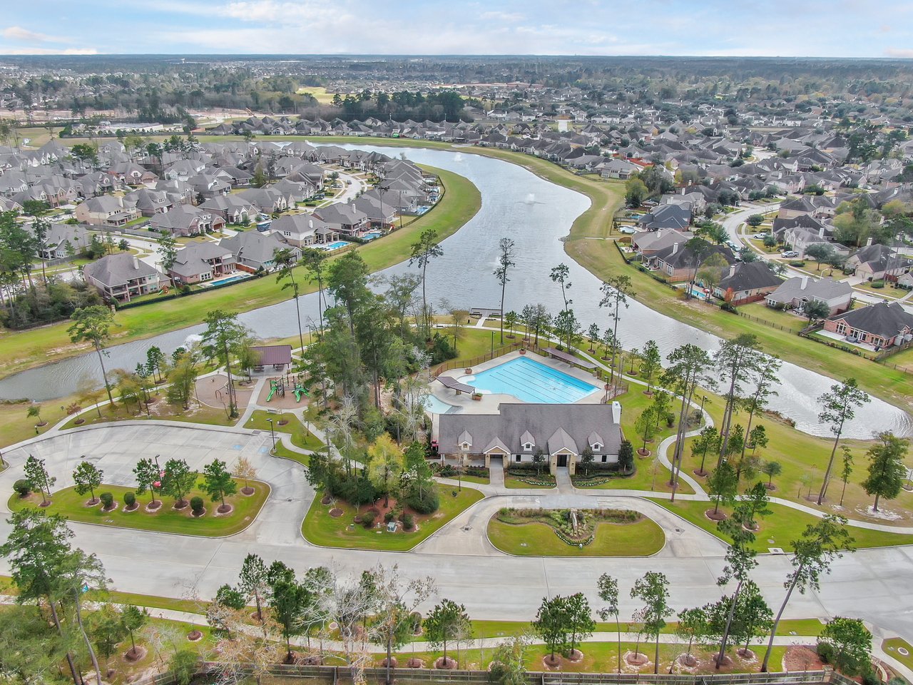 Aerial view of a neighborhood lake and homes surrounding a community pool and playground.