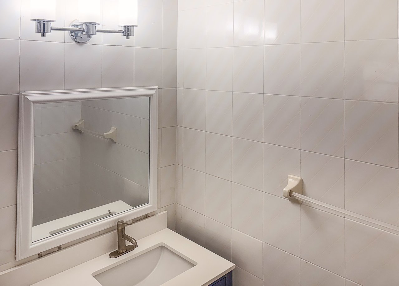 Bathroom vanity with a framed mirror, white sink, chrome faucet, and pale tiled walls.