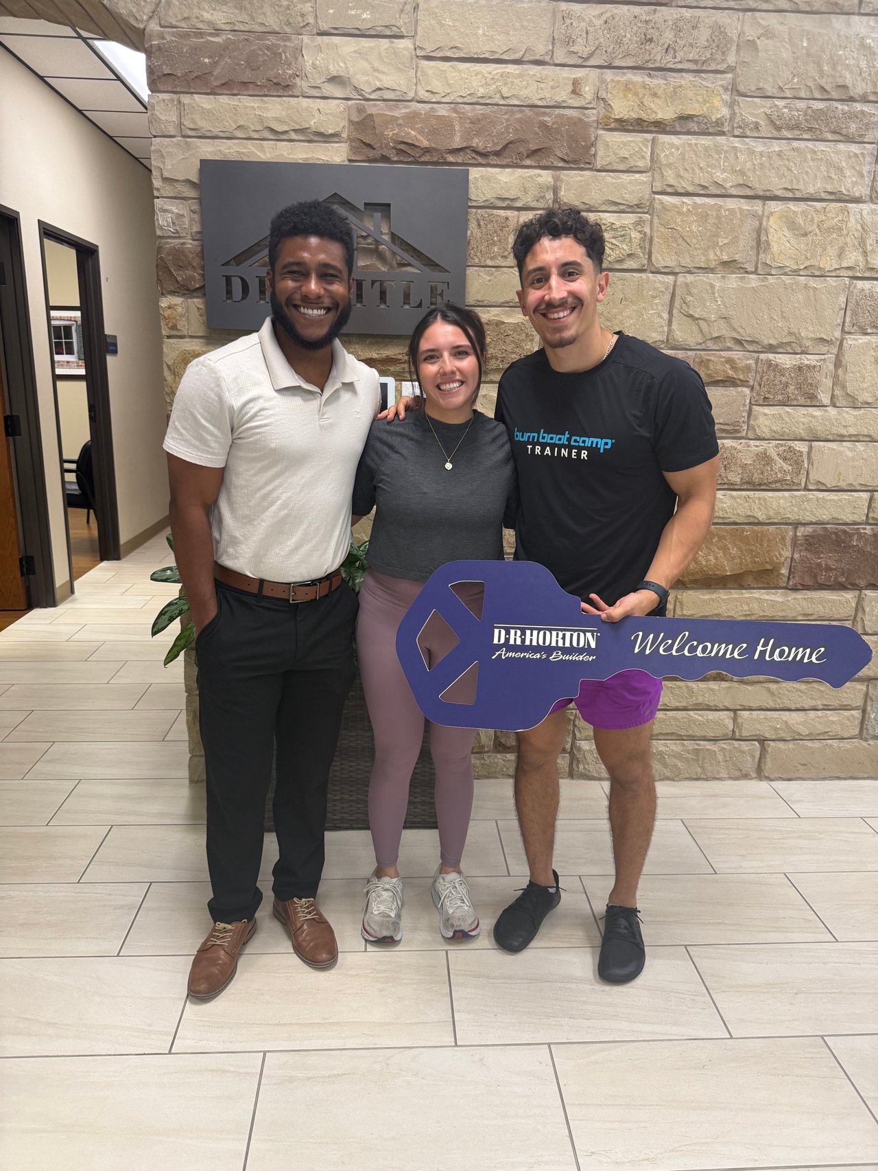 Three adults pose with a purple D.R. Horton Welcome Home key sign.