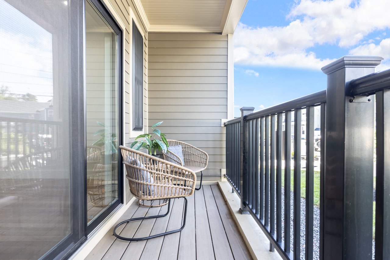 Covered balcony with wicker chairs, gray decking, and black railing.