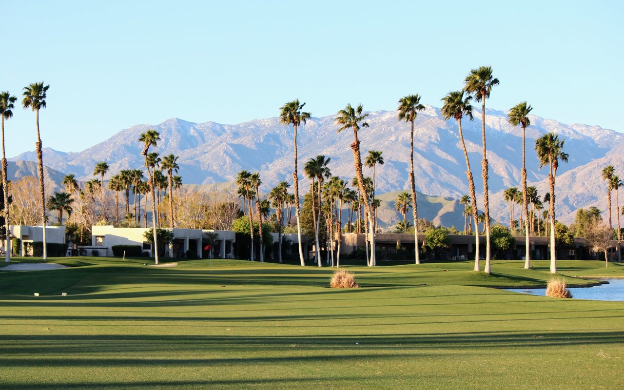 Golf course with palm trees, a pond, and mountains in the background.