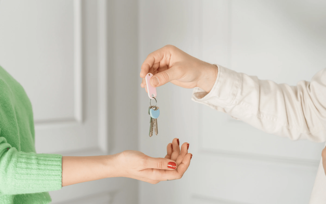A person in a green sweater reaches to receive house keys from another person.