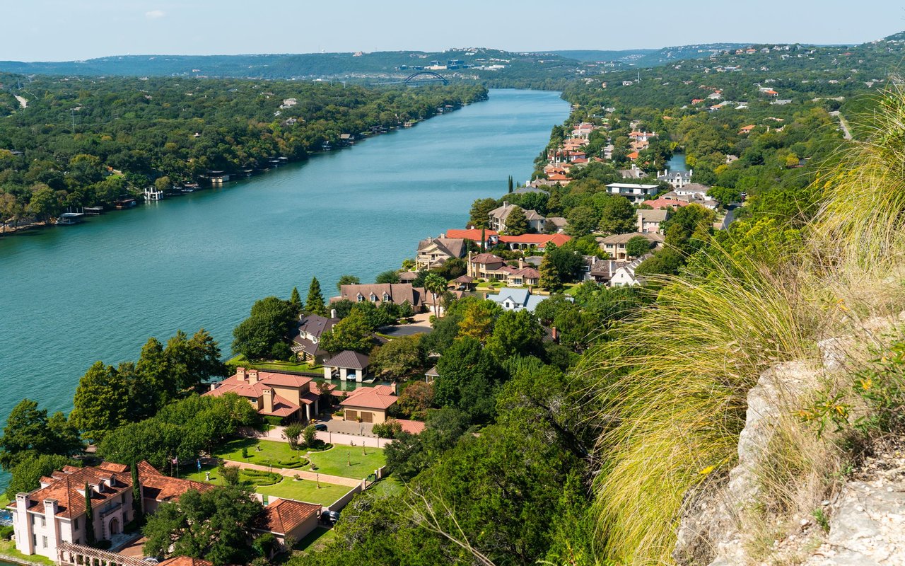 Lake Austin bordered by wooded hills and shoreline homes, viewed from above.