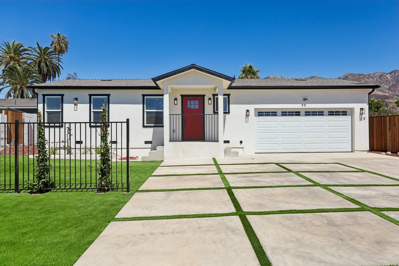 White single-story home with a red front door, two-car garage, and grass-strip driveway.
