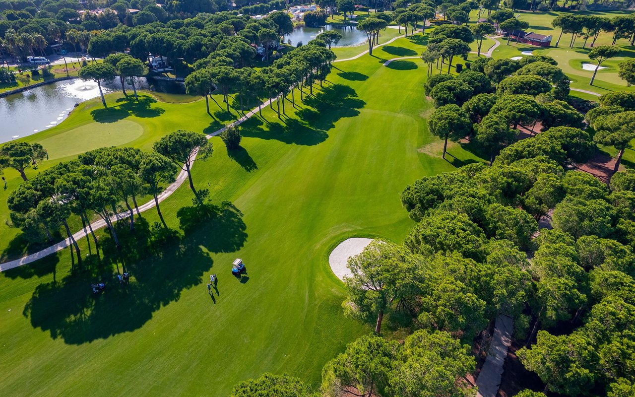 Aerial view of a tree-lined golf course with broad fairways, sand bunkers, and a pond.