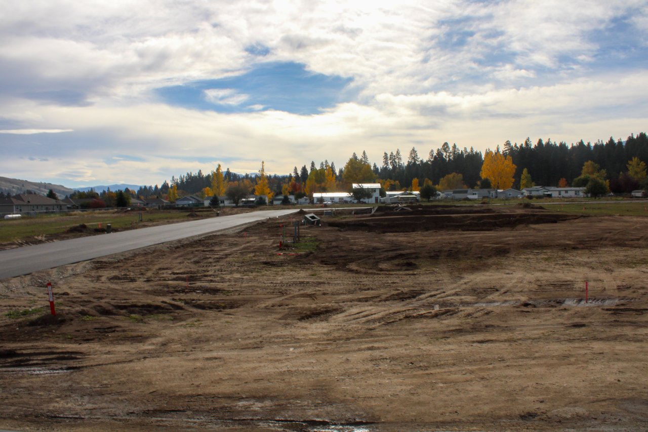 Developing subdivision with graded lots, a paved road, and autumn trees.
