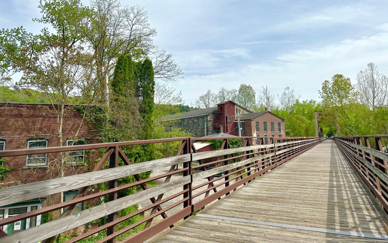 Farmington River Trail bridge in Connecticut, featuring a scenic walkway over the river surrounded by trees and natural beauty, popular for biking and walking.