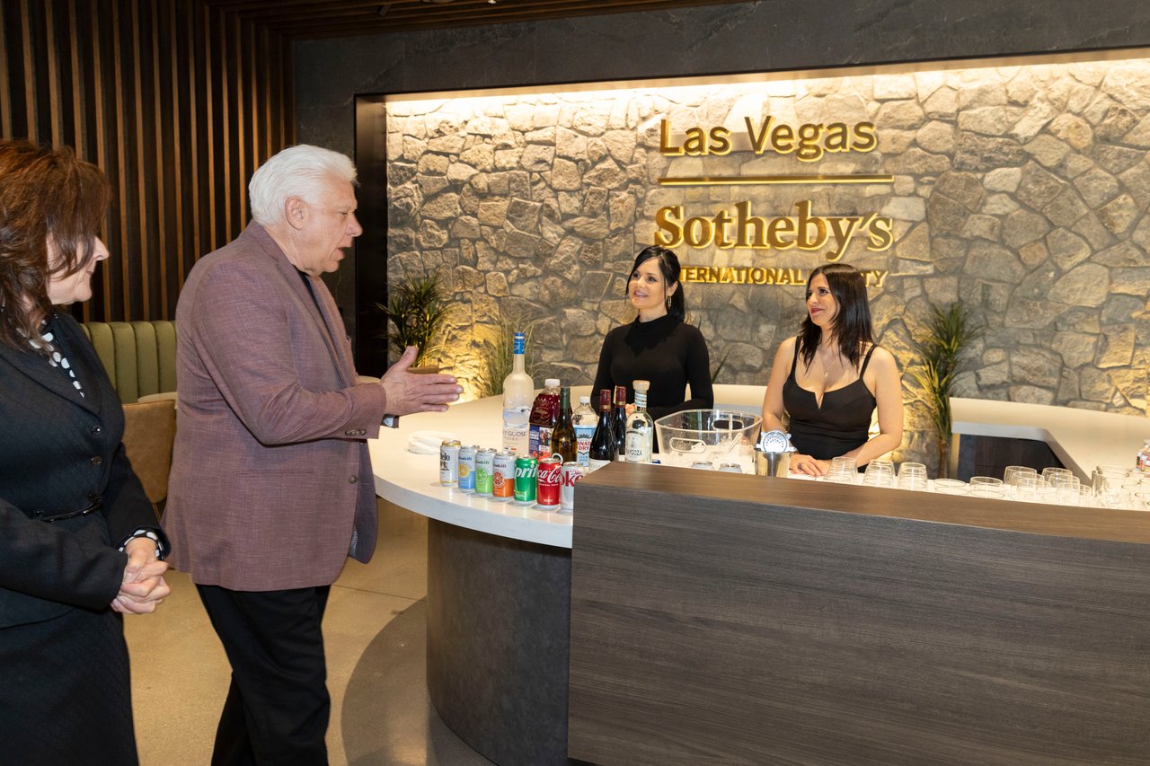 Guests and staff gather at a drinks counter beneath a Las Vegas Sotheby's International Realty sign.