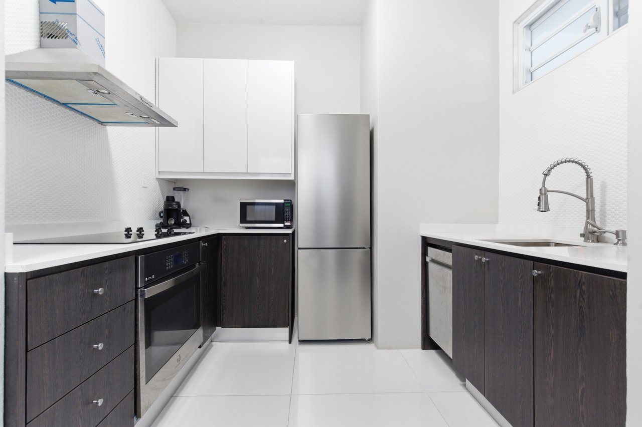 Modern kitchen with dark cabinets, stainless steel appliances, and white countertops.