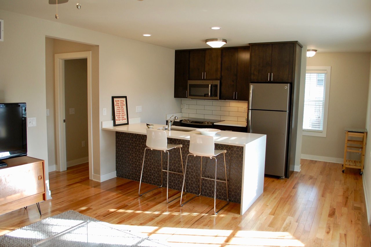 Furnished apartment kitchen with dark cabinets, stainless steel appliances, and a white island with two stools.