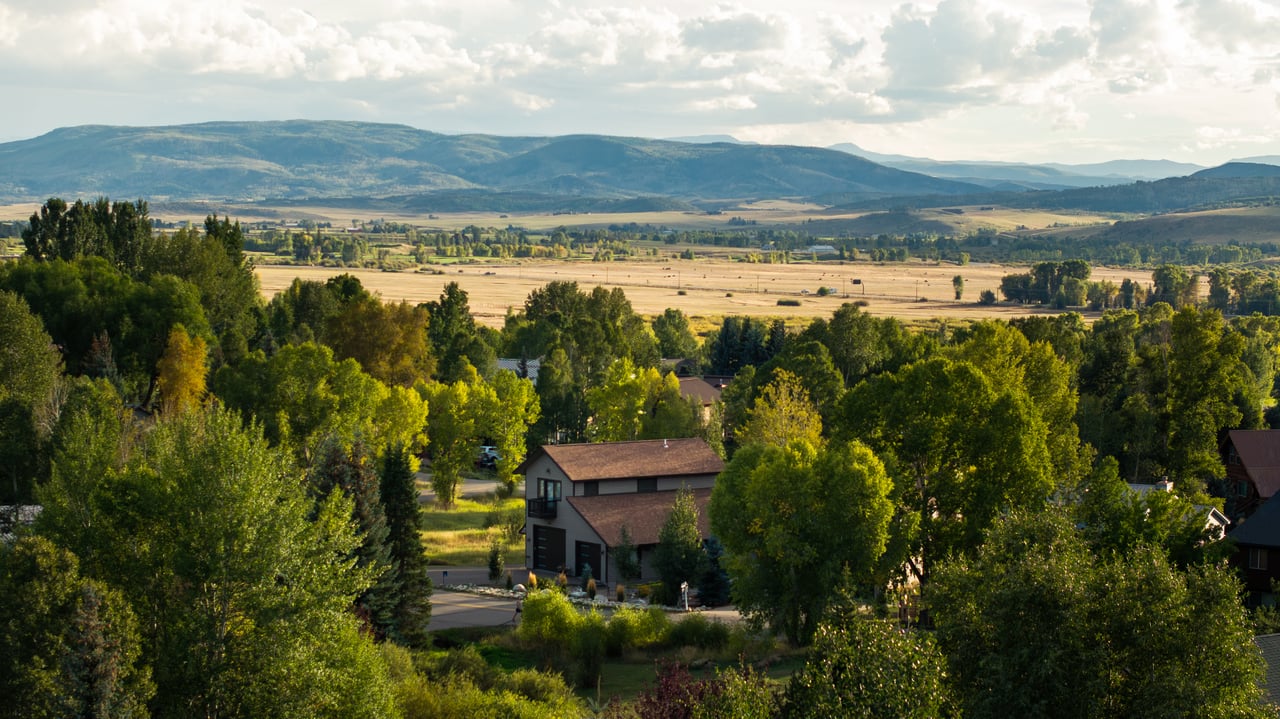 House among trees with a wide valley and mountain range beyond.