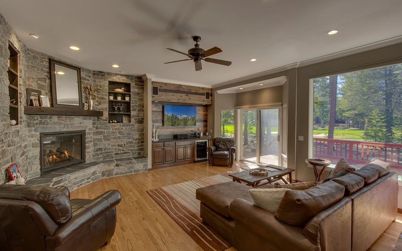 Living room with a stone fireplace, leather seating, and sliding doors to a wooded deck.