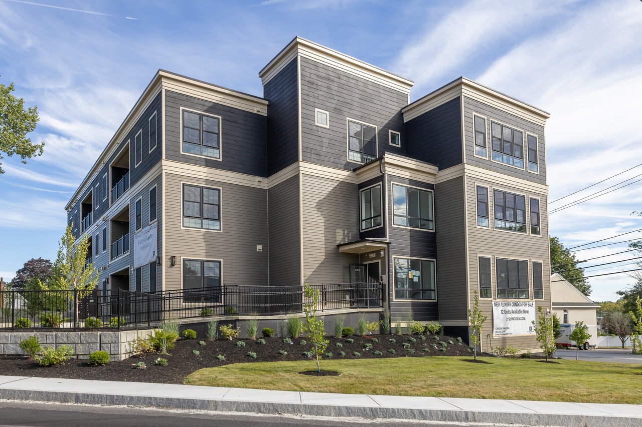 Modern gray condominium building with landscaped frontage and a new-condos-for-sale sign.