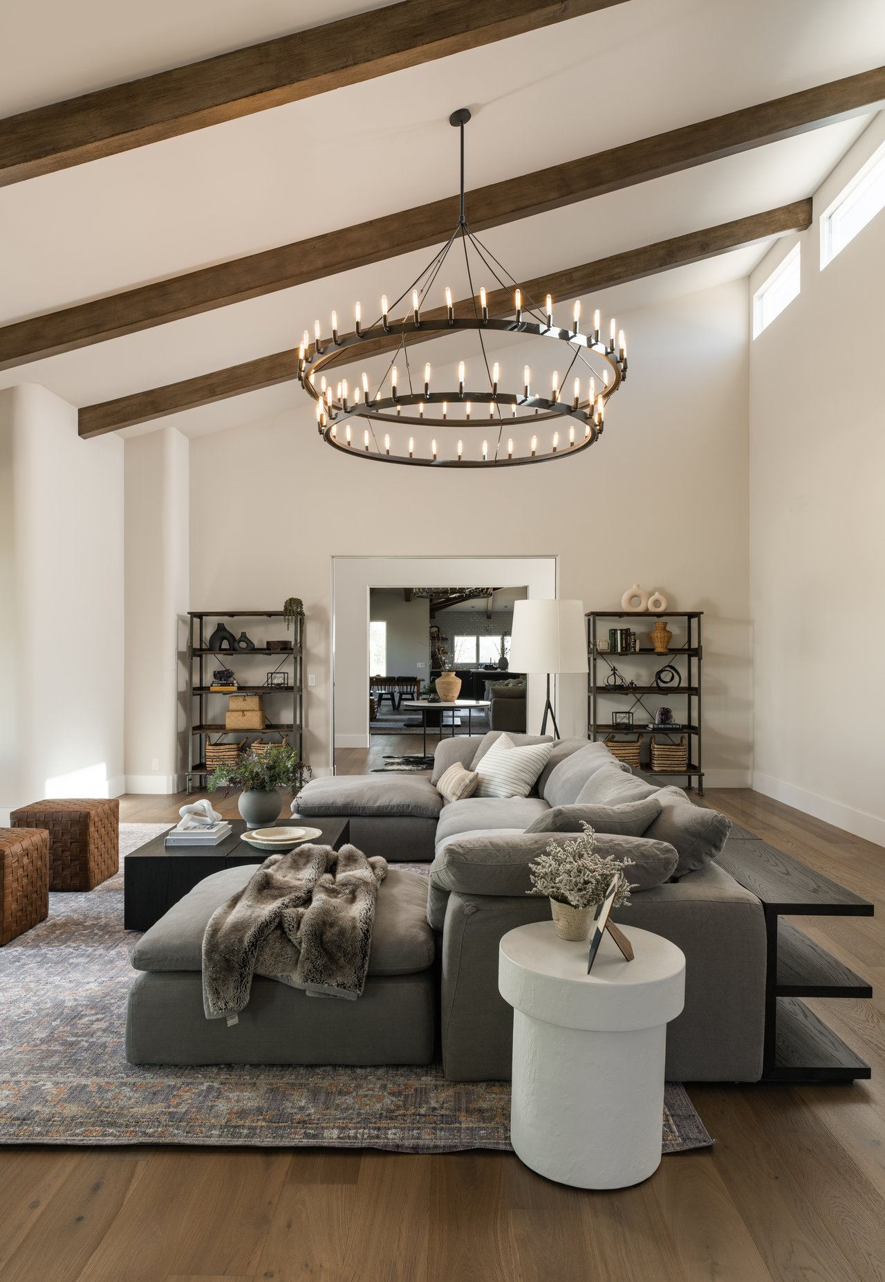 Vaulted living room with exposed wood beams, a tiered chandelier, and a gray sectional sofa.