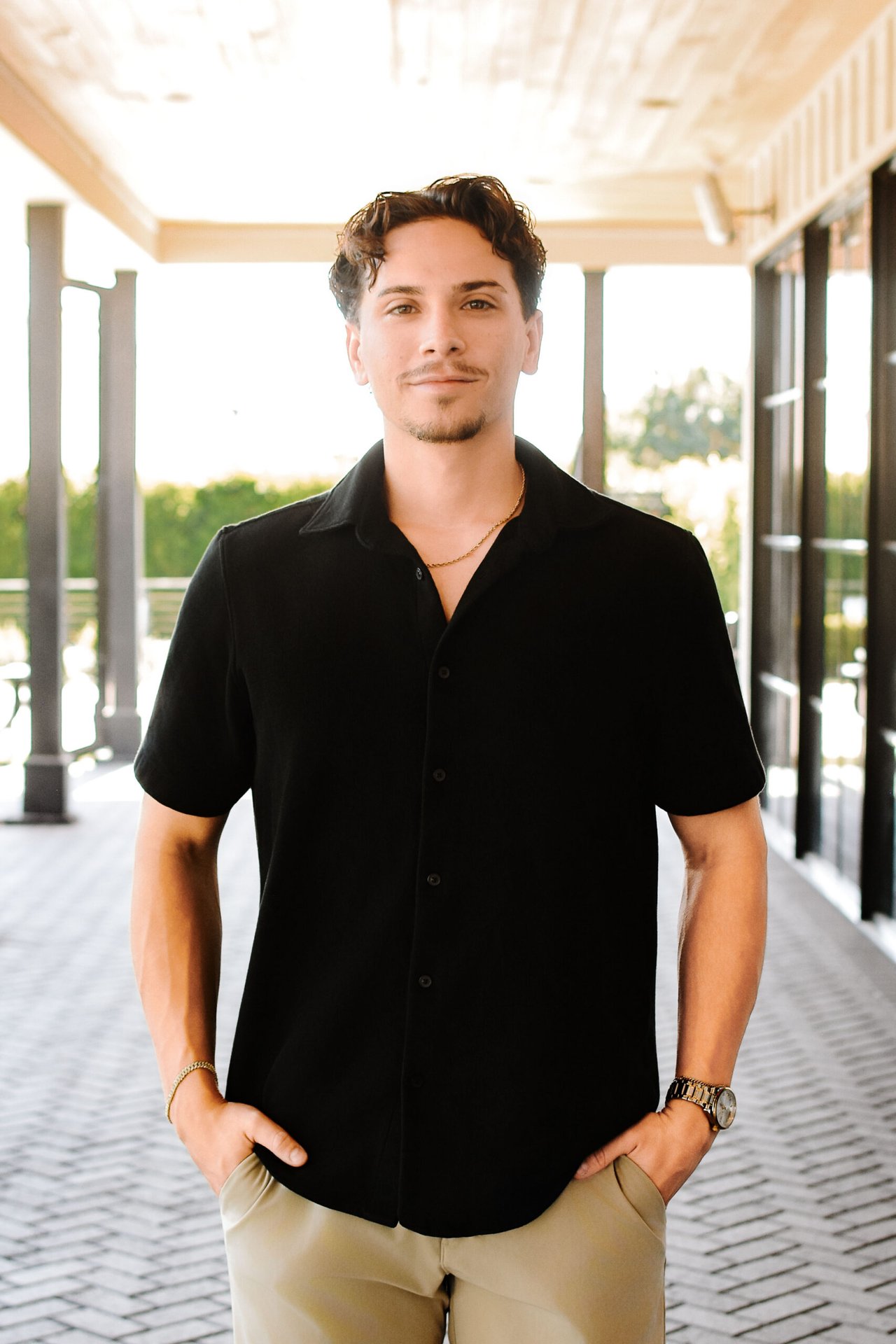 Cade Verdusco in a black shirt and tan trousers on a covered outdoor walkway.