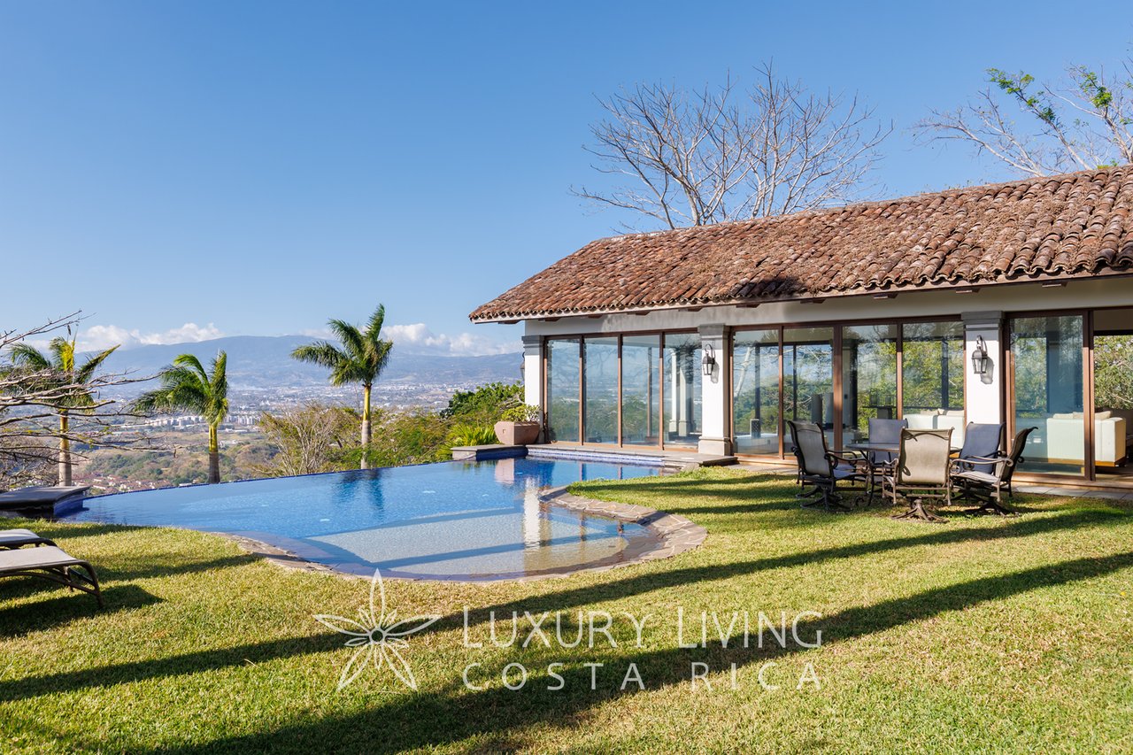 Luxury home beside a curved pool, with a broad lawn and distant mountain views.