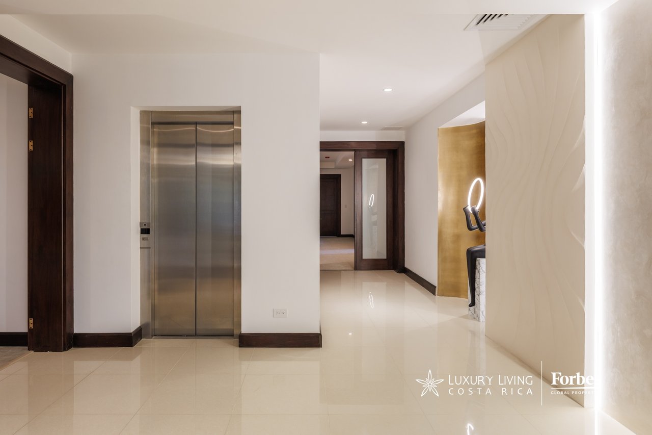 Penthouse hallway with a stainless-steel elevator, glossy tile floors, and dark wood trim.
