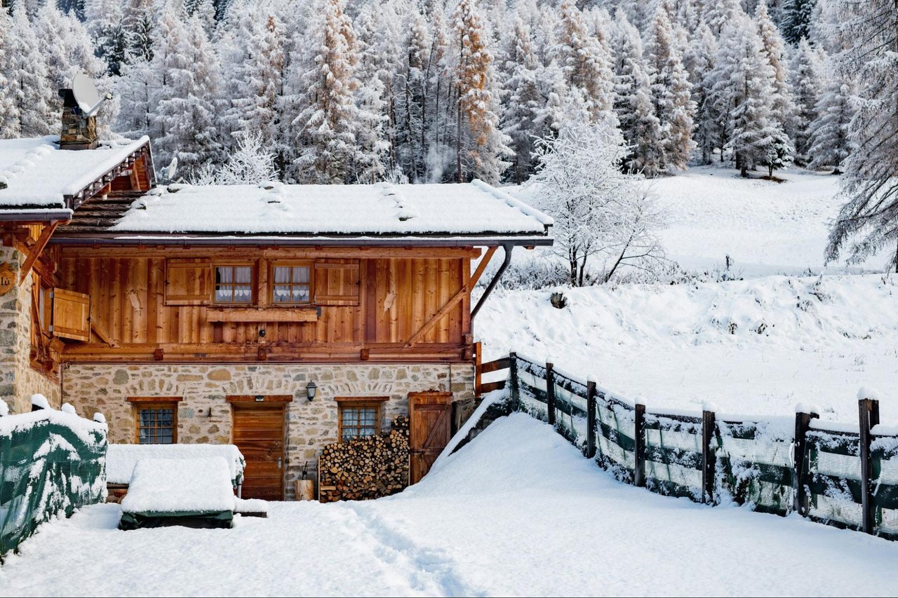 Wood-and-stone mountain home surrounded by deep snow and frosted trees.