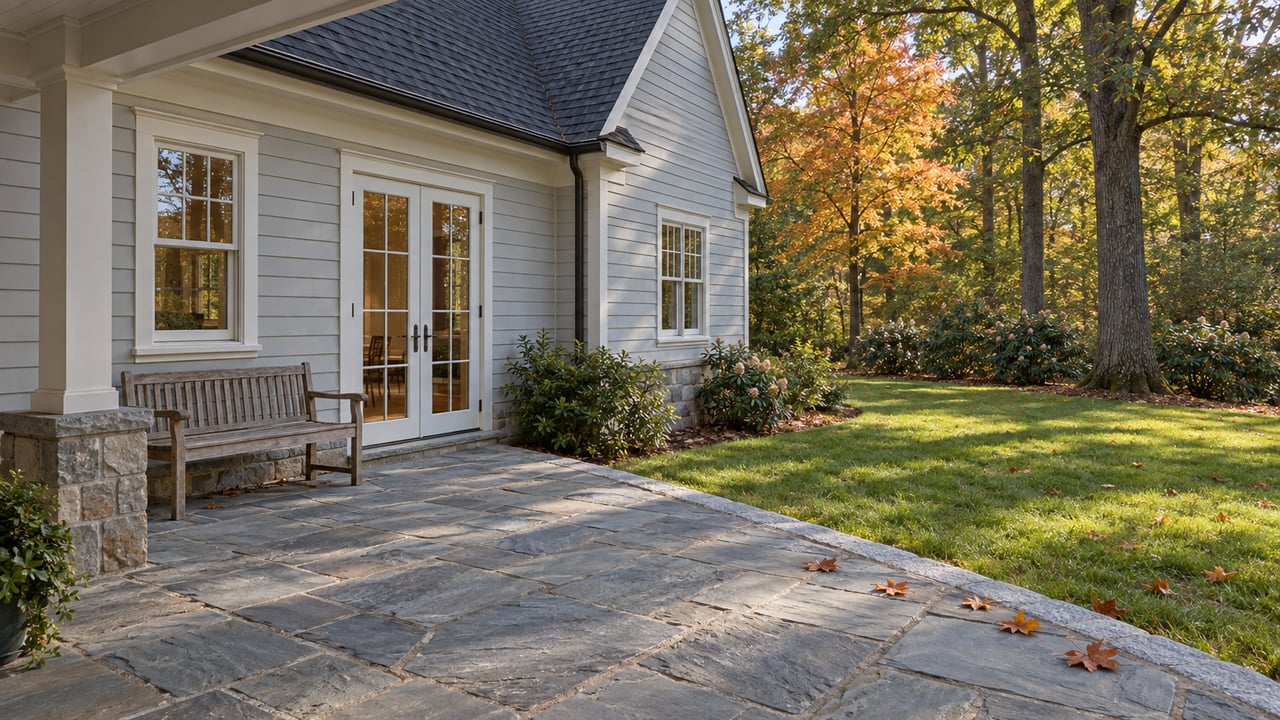 House exterior with a stone patio, French doors, wooden bench, and autumn trees.
