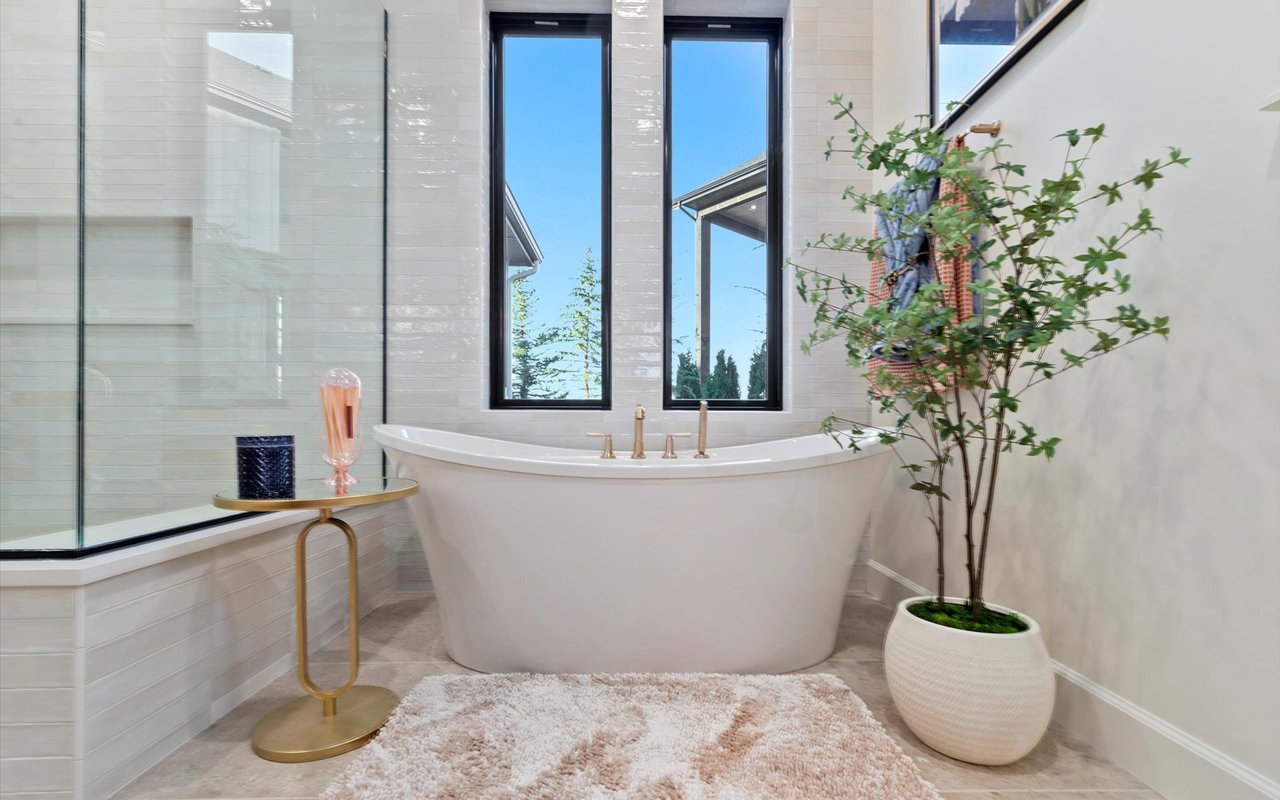 Close-up of the primary bathroom soaking tub in front of two tall windows overlooking the backyard trees