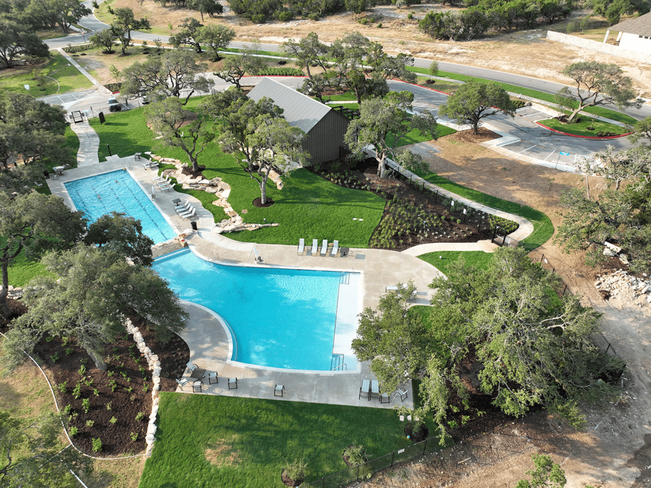 Aerial view of two connected community pools surrounded by lawns, trees, and walking paths.