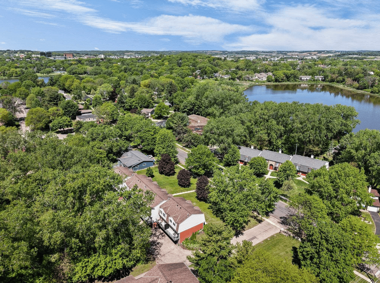 A scenic aerial view of Middleton, Wisconsin, showcasing established suburban neighborhoods surrounded by lush green tree canopies and a tranquil local lake, highlighting the premium lifestyle of the Good Neighbor City.