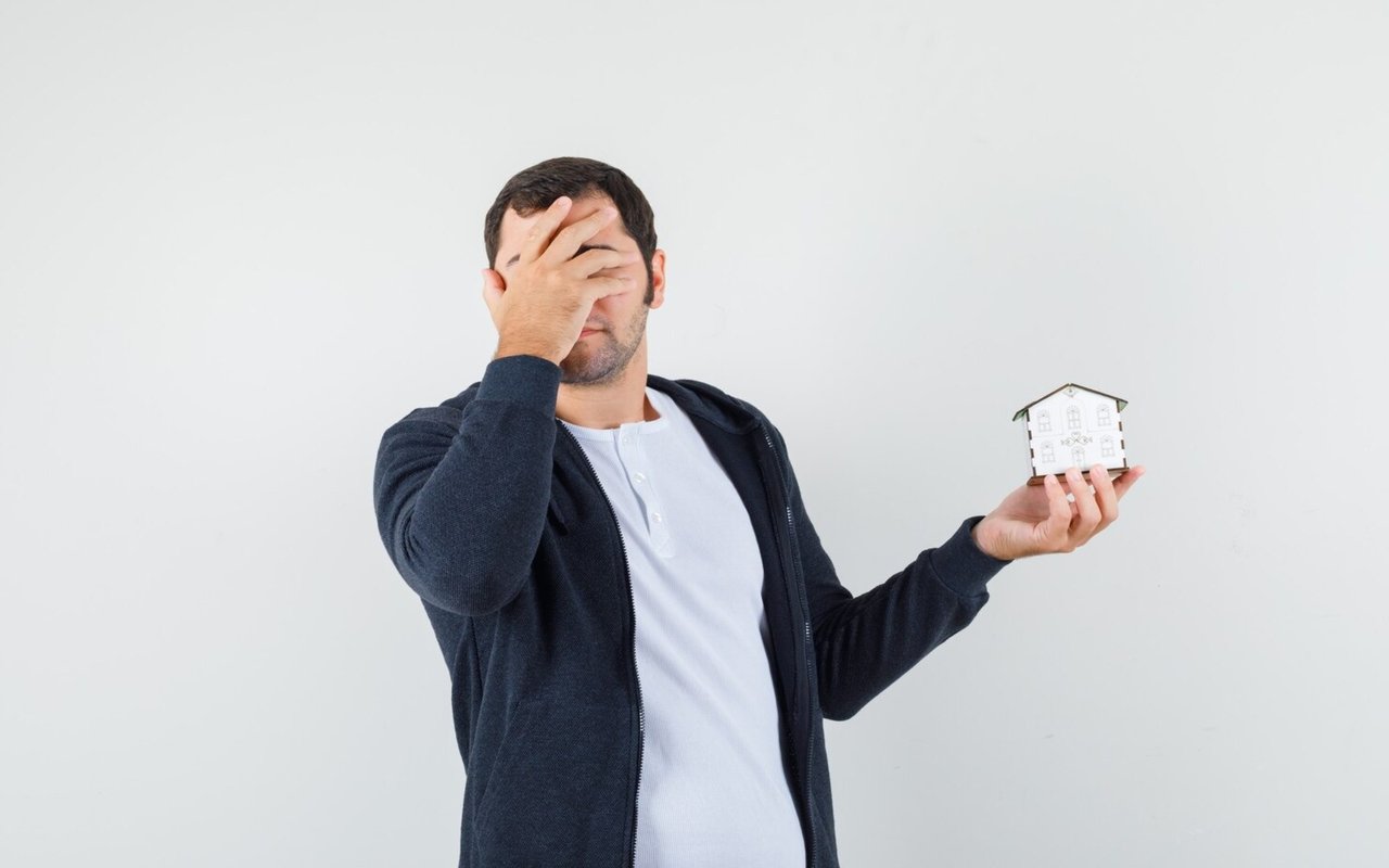 Man covering his face while holding a small model house