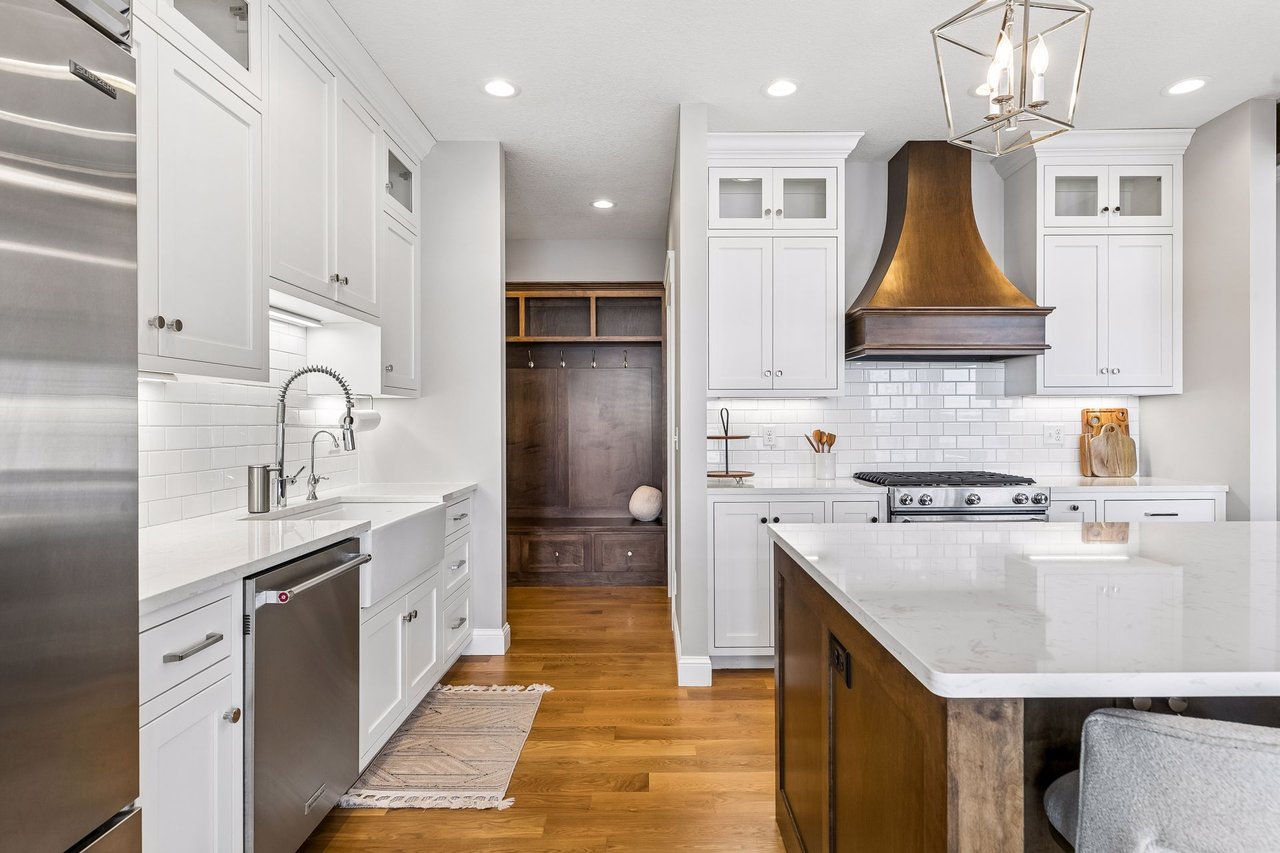 Bright kitchen with a large island, white cabinetry, copper range hood, and dark wood built-in bench.